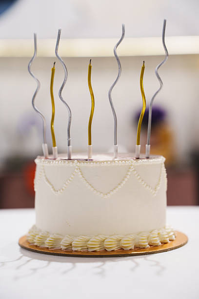 Birthday cake with burning candles on pink background with many colorful sprinkles.