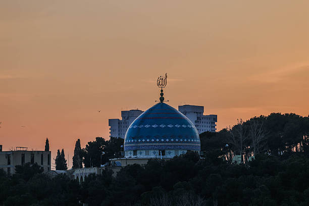 Prominent mosque dome surrounded by city buildings in Tehran during warm sunset light. Blend of religious architecture and modern urban landscape.