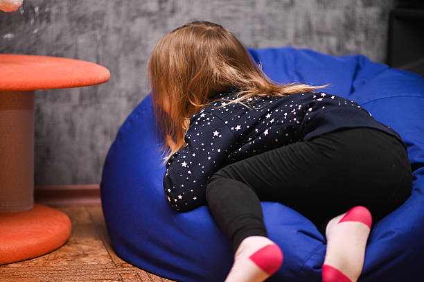 Young schoolgirl sitting in a comfortable beanbag, smiling joyfully against a pink background. The scene exhibits relaxed and cheerful vibes.