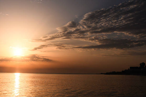 Sunset paints sky and sea in warm orange hues. Calm ocean perfectly mirrors brilliant colors. serene scene of evening tranquility over water. Golden sunlight shimmers across calm sea at sundown.