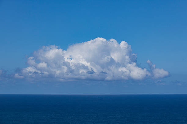 Single large cumulus cloud floating above the deep blue ocean horizon under clear sky conditions. The minimalist seascape captures open water and sky with ample copy space.