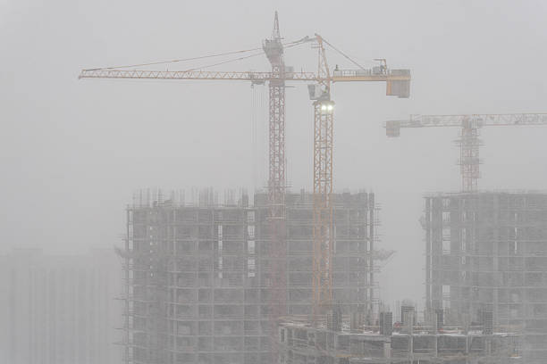 Residential buildings under construction with tower cranes in winter fog conditions. Suitable for urban development and real estate background use.