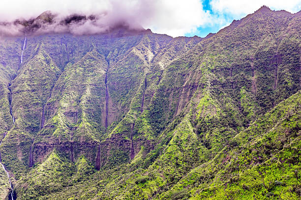 A vintage 1980s film photograph aerial view of the lush green Hawaiian hills in the Honopu ridge valley in Kauai from a helicopter with lush blue ocean water in the background.
