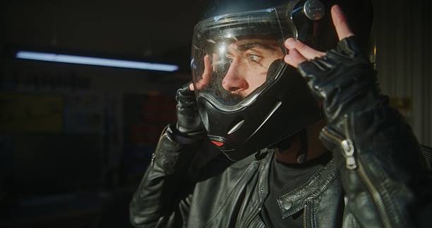 Close Up of Young Motorcyclists Face Prepares For Ride in Private Garage. Male Securing Chin Strap and Lowering Visor. Concept of State of Total Concentration Pilots Ready For Road. Slow Motion.