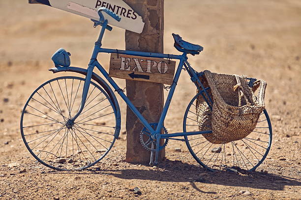 A Dilapidated, old blue bicycle leaning on a stone masonry pillar serves as a signpost to indicate a painters' workshop and expo, in the village of Khamlia at the foot of Erg Chebbi. Merzouga-Morocco.