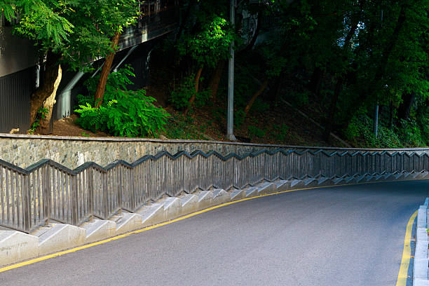 A winding road bordered by a unique wooden fence and dense foliage, suggesting a path through nature or an urban park setting