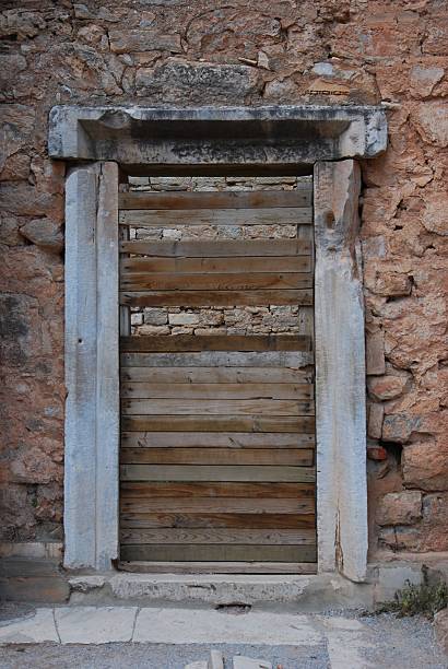 A vertical, eye-level shot of a classical marble doorframe integrated into a rough-hewn stone wall. The entrance is sealed with aged timber planks, blending ancient masonry with rustic temporary repairs. Ideal for themes of archaeology, history, and architectural preservation.