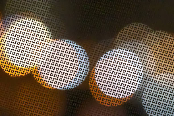 Warm and cool round bokeh lights shining through a dark metal mesh grid create a geometric pattern of blurred circles with copy space for minimal digital nomad background design and tech vibe.