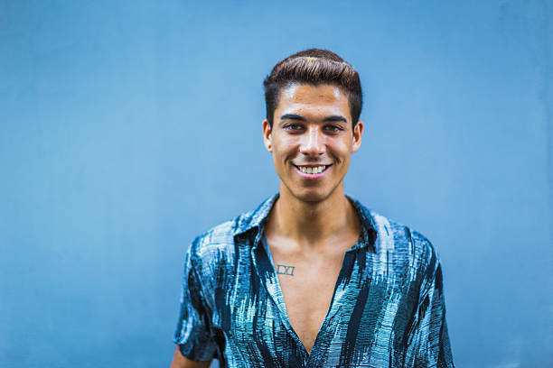 Portrait of a young man in a blue shirt smiling against a blue background.