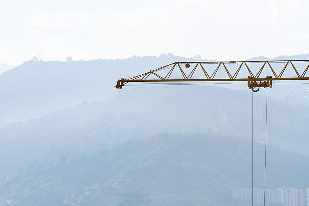Tall yellow tower crane at a construction site with urban buildings and mountain landscape in the background. Concept of urban development, infrastructure growth, real estate expansion and modern city construction