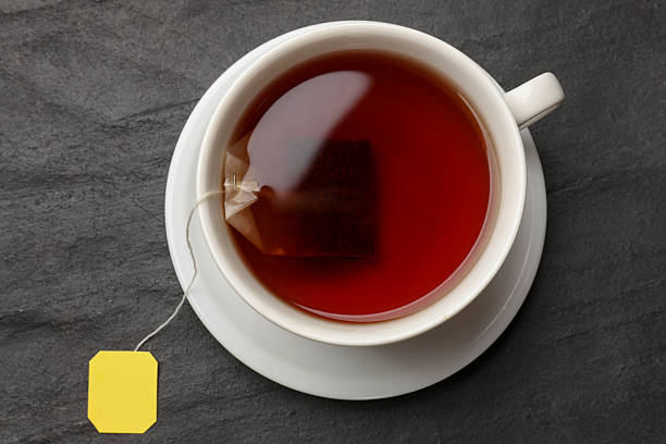 Tea bag in cup with hot drink on grey textured table, top view