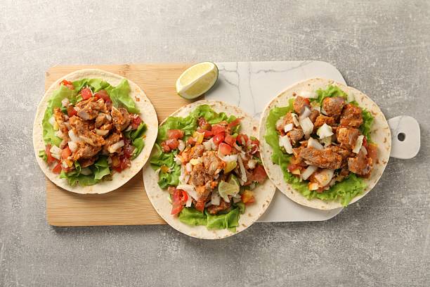 Delicious tacos with vegetables, meat and lime on grey textured table, top view