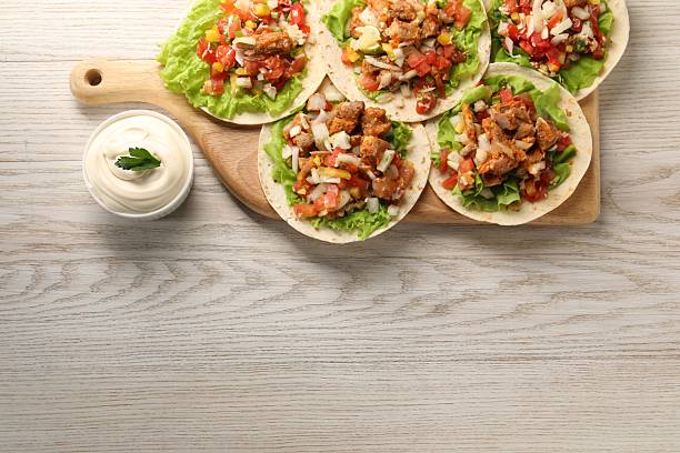 Delicious tacos with vegetables, meat and sauce on white wooden table, top view. Space for text