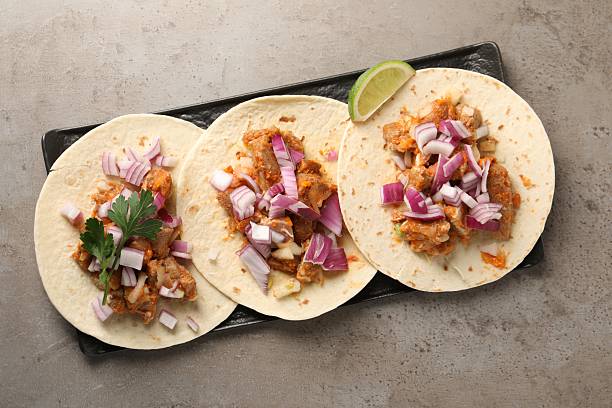 Delicious tacos with vegetables, meat and lime on grey textured table, top view