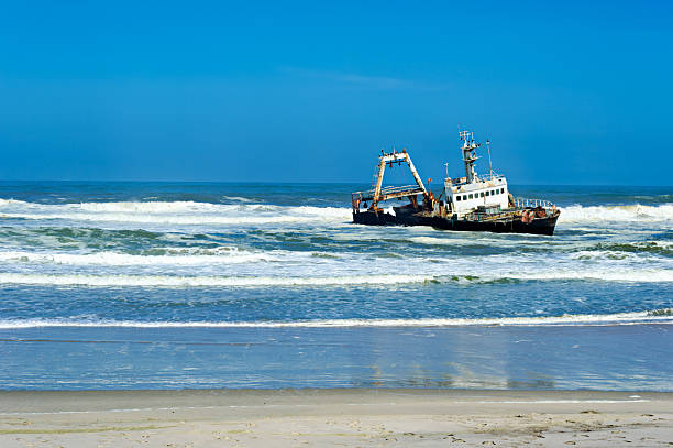 A shipwreck sits stranded on the Skeleton Coast of Namibia. Waves crash around the vessel, showing the harsh conditions of the Atlantic Ocean.