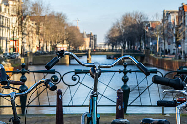Bicycles parked on a bridge railing overlooking a canal with traditional dutch architecture and bare trees line the city streets under clear skies, capturing the essence of european urban travel