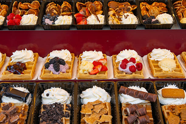 Assortment of fresh dutch waffles and small poffertjes pancakes with various sweet toppings like whipped cream, fruits, chocolate, and jam celebrating traditional street food