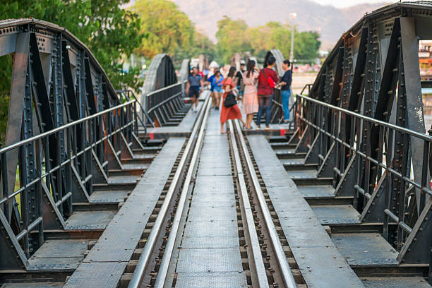 Unrecognizable people walking by rail track of old railroad bridge on river Kwai. Kanchanaburi, Thailand