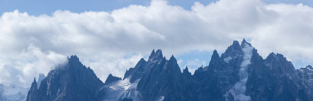 Sharp rocky summits of Aiguille de Blaitiere emerge through drifting clouds, with patches of lingering snow and dramatic textures in the French Alps.