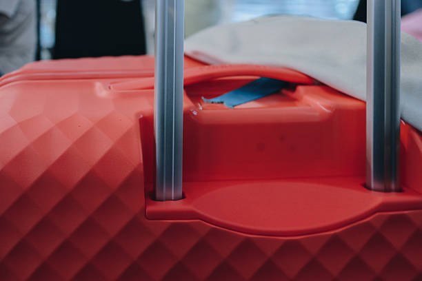 A detailed view of the top of a red suitcase, showing the retractable handle mechanism and the patterned exterior.