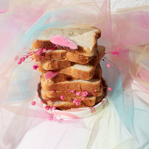 Stacked bread slices with pink flowers on pastel pink tulle fabric, surreal still life.