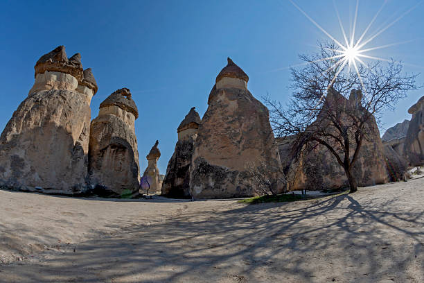 A dramatic wide-angle shot of volcanic fairy chimneys in Pasabag Valley with a beautiful sunburst effect under a clear blue sky, Nevsehir, Turkey.