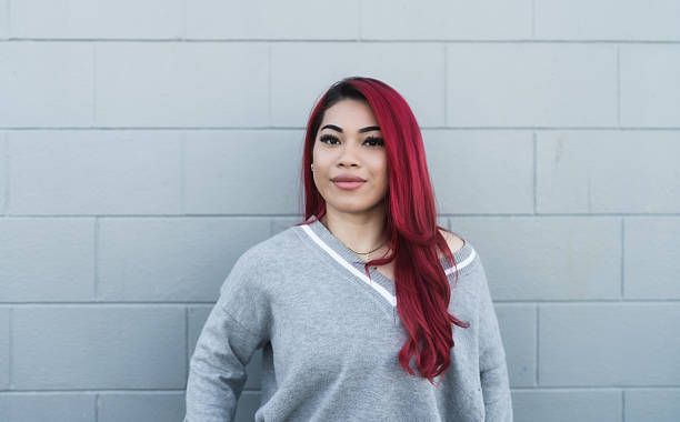Portrait of a self-assured Maori woman standing against a grey wall, showcasing confidence, elegance, and contemporary style in a clean, minimalist setting.