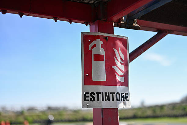 Red Estintore sign displaying fire extinguisher symbol on metal pole under blue sky