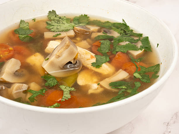 Close-up of Tom Yum Kha soup with mushrooms and herbs on marble