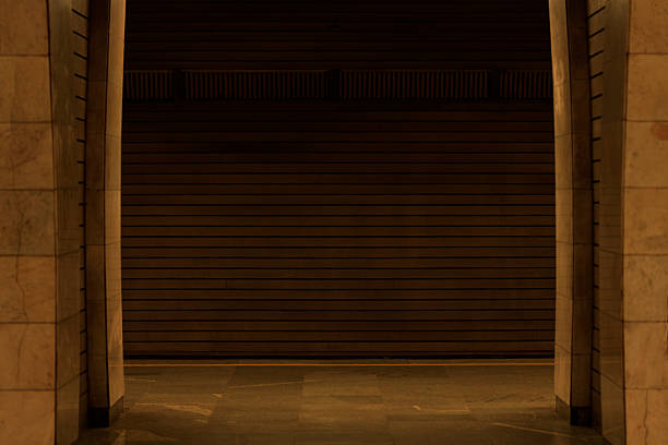 An atmospheric view of a deserted metro station platform, featuring textured marble pillars and a dark, horizontally paneled wall