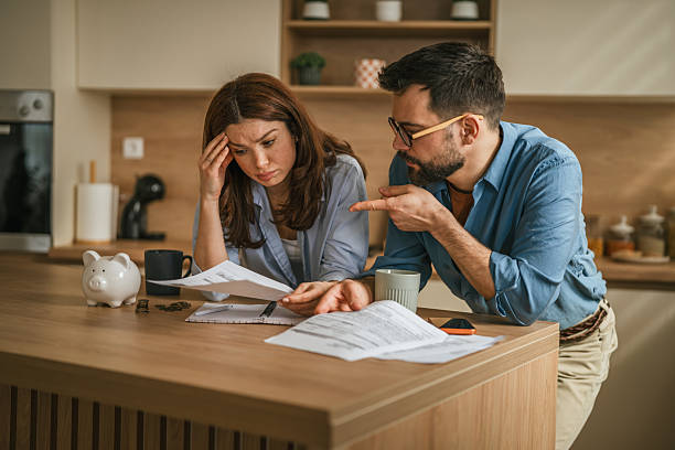 Stressed young couple managing bills and financial problems at home Stressed young couple sitting at a kitchen counter, discussing financial problems while reviewing bills and documents, holding head in hand in frustration, with a piggy bank nearby tax planning discussion stock pictures, royalty-free photos  images