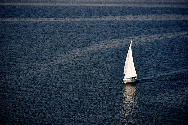 At sunset, a single-masted sailboat on a blue sea