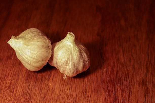 Collection of fresh whole garlic bulbs arranged on a rustic wooden surface in different compositions, including close-up details and natural peel textures. Concept of organic food, healthy cooking, natural ingredients, immune support, and traditional home kitchen preparation.