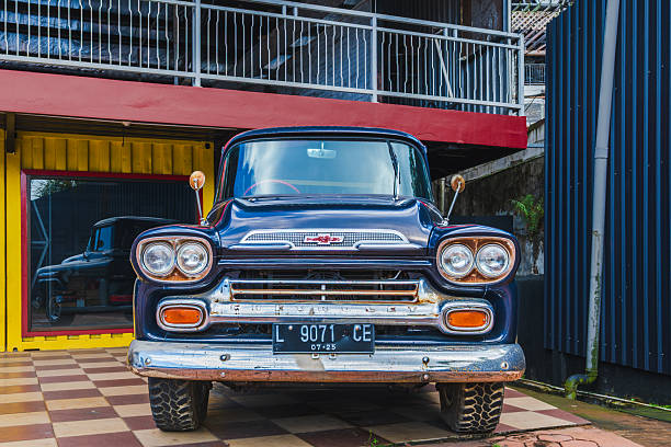 Balikpapan, Indonesia - December 10, 2025. Vintage Blue Chevrolet Apache Pickup Truck Parked in Front of a Modern Container Building
