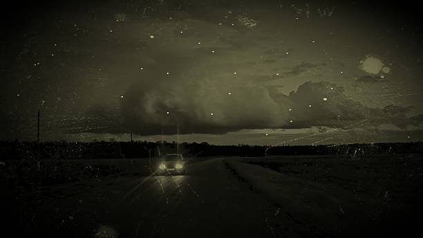 Retro Vintage Car on Dark Rural Road Under Starry Night Sky. Vintage retro effect: lonely car drives empty rural road at night, headlights piercing darkness under dramatic starry sky with swirling clouds.