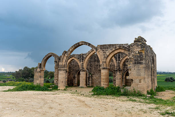 Remaining stone arches of agios sozomenos church ruin standing against a dramatic sky in a rural landscape