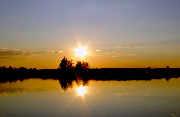 Bright golden sunset with sunstar reflection on calm lake