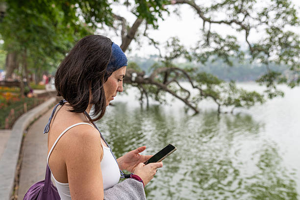 Woman messaging on smartphone, standing by hoan kiem lake, experiencing connectivity during travel hanoi vietnam