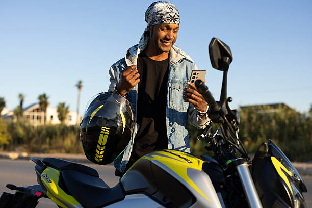 A mature man is preparing for riding his motorcycle. He is setting his helmet after relaxation on the road through the nature