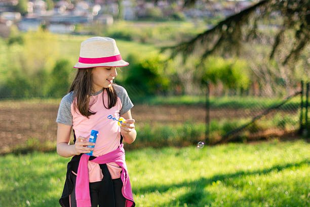 Young girl smiling, blowing soap bubbles in a sunny outdoor setting, embodying childhood joy and freedom
