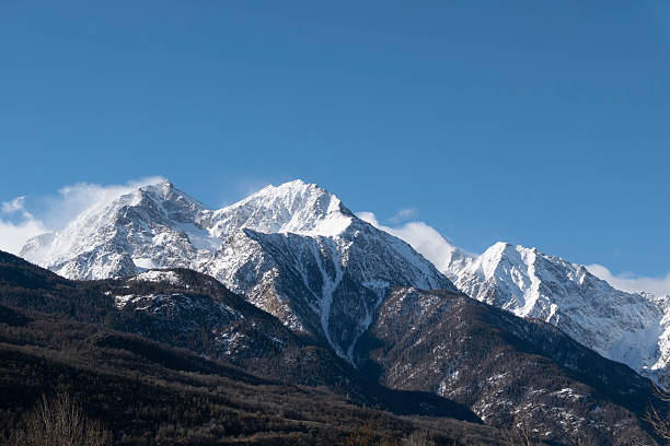 Dramatic snow-covered mountain ridge in the Italian Alps with sharp peaks and wind-shaped snow formations under deep blue sky. Scenic winter alpine landscape showcasing rugged terrain and pristine winter conditions.