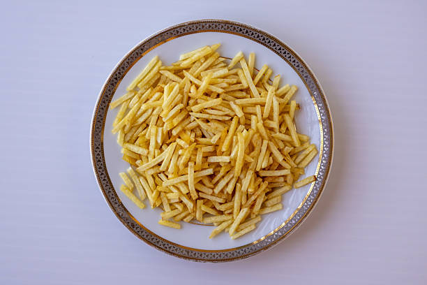Close-up of crispy golden potato sticks on a white plate. Crunchy deep-fried salted matchstick fries isolated on white background. Savory snack and appetizers for food photography. Top view