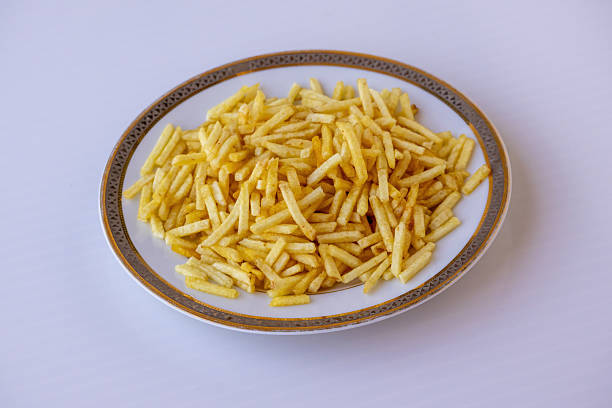 Crispy golden potato sticks served on a white plate over a white background. Close-up of crunchy deep-fried salted matchstick fries, a savory snack perfect for fast food and catering concepts