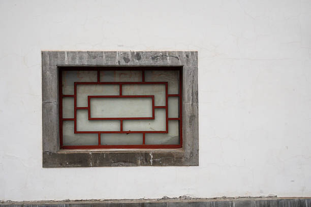 A traditional Chinese lattice window with red patterns on a white exterior wall, showcasing architectural design and cultural heritage.