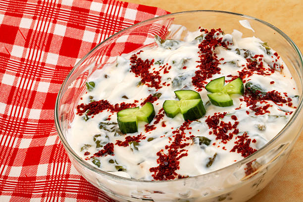 Cacik with chopped cucumber and red pepper flakes in a clear glass bowl, top view, natural light, centered composition.