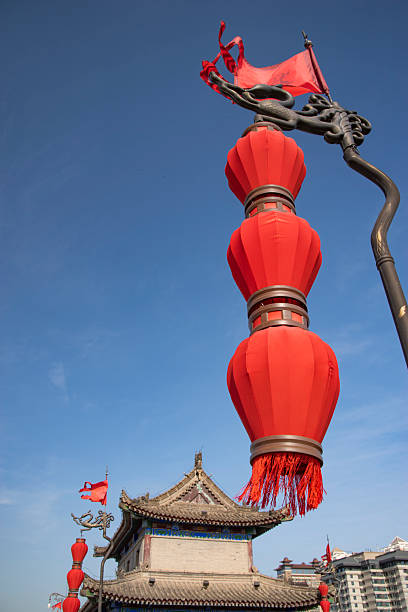 Row of iconic red lanterns hanging from dragon-shaped lamp posts on the Xi'an City Wall. This Ming Dynasty heritage site offers a stunning contrast between ancient fortifications and the modern skyline of Xi'an, Shaanxi province, China