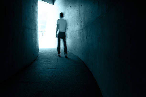 Single man walking in narrow and dark corridor to glowing lights