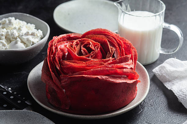 Red velvet pancake cake shaped like a large rose with cream cheese filling, served with cottage cheese and milk. Traditional Maslenitsa or Valentine's Day dessert.