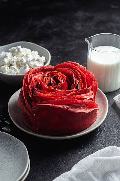 Red velvet pancake cake shaped like a large rose with cream cheese filling, served with cottage cheese and milk. Traditional Maslenitsa or Valentine's Day dessert.