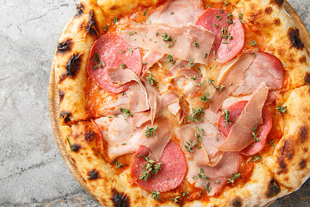 Crispy charred meat pizza with prosciutto, salami, bacon and ham close-up on a wooden board. Horizontal top view